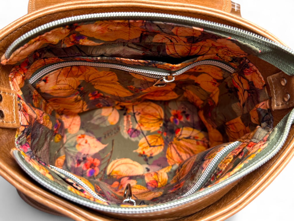 Top view of a tan leather handbag with flap open showing interior and botanical lining of Belle bag.
