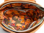 Top view of a tan leather handbag with flap open showing interior and botanical lining of Belle bag.
