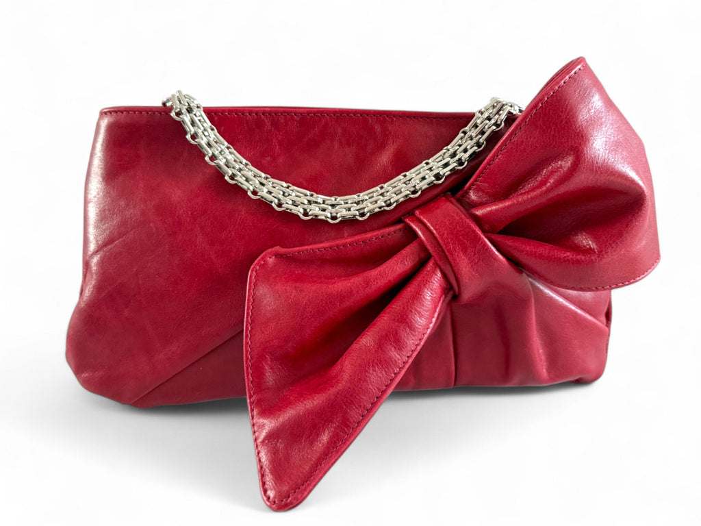 Red leather Betty Bow clutch bag with a large bow and silver bracelet chain detail on a white background. 