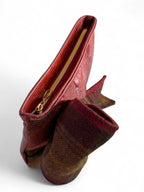 Bird's Eye view of a burgundy leather and plaid tweed clutch bag with a gold zipper on a white background