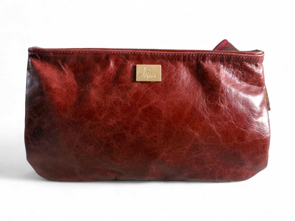 View of the back of a deep red leather clutch bag with a gold tag on a white background