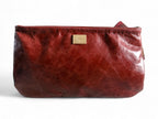 View of the back of a deep red leather clutch bag with a gold tag on a white background