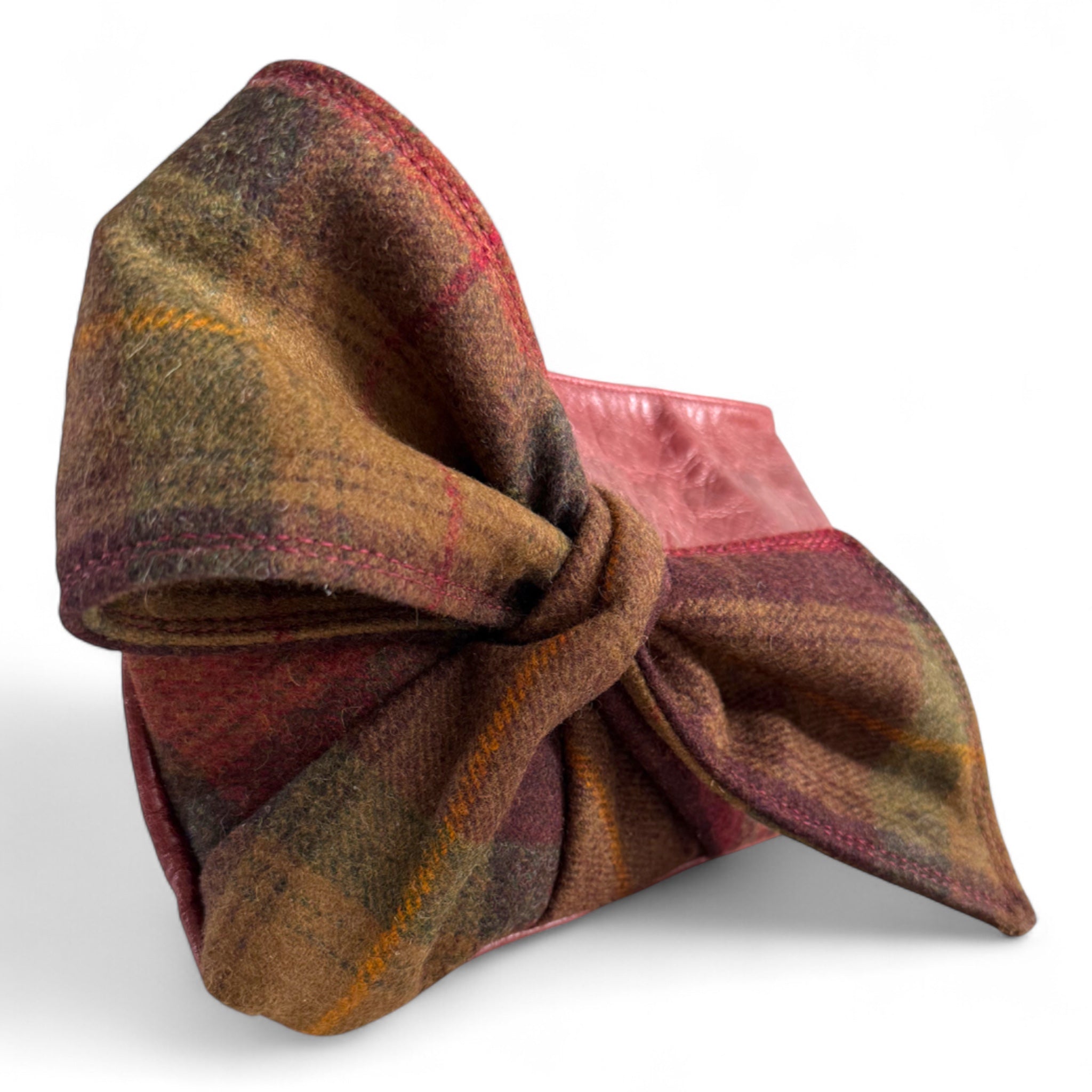 Close up view of the pllaid tweed bow with a knot on the front of a burgundy leather clutch bag on a white background