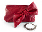 Red leather clutch with a large bow and a silver bracelet style removable chain strap on a white background. 