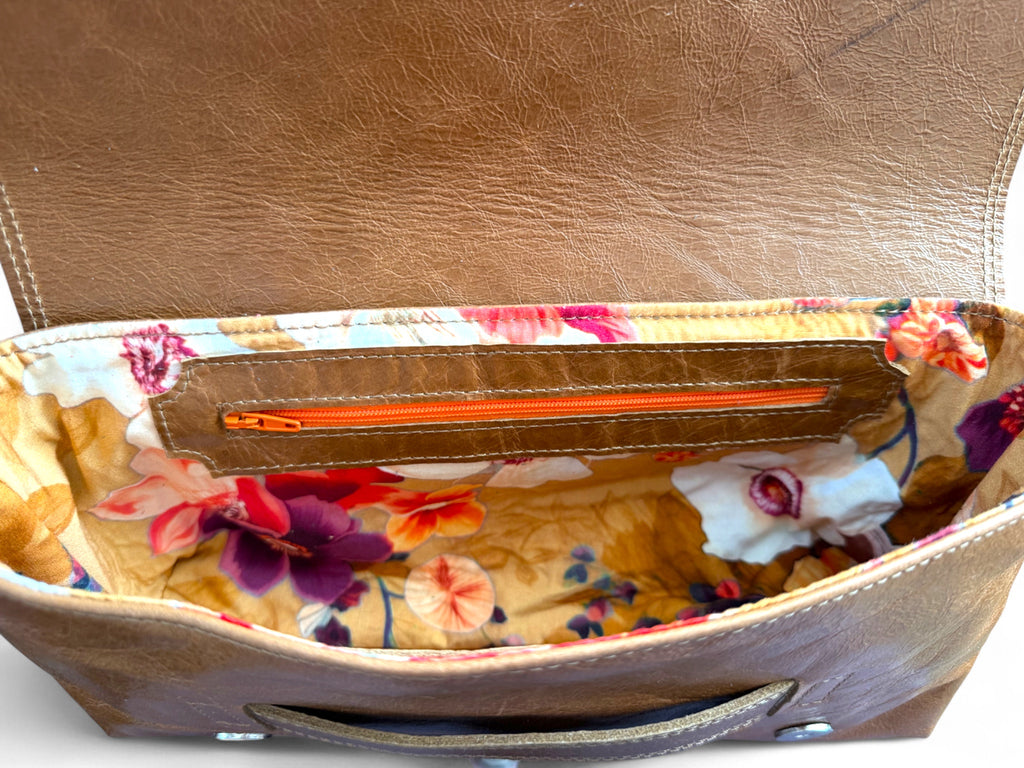 Open brown leather handbag with floral interior lining. 