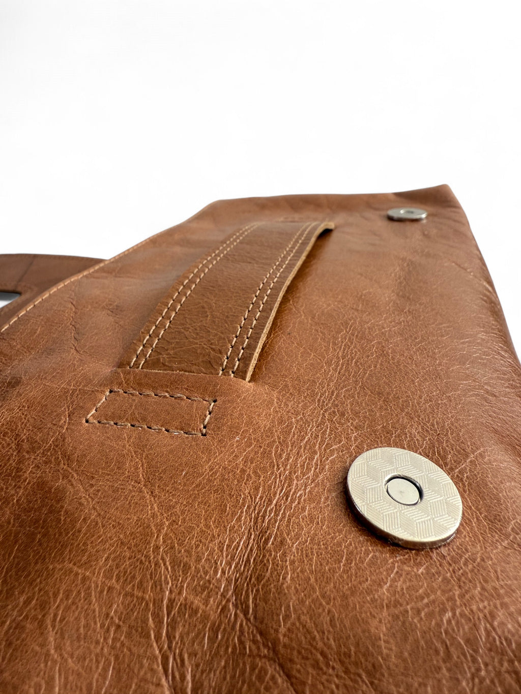 Close-up of the tan brown leather Bronte clutch bag with stitching details on the slip handle and the silver metal magnetic clasp. 