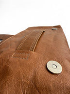 Close-up of the tan brown leather Bronte clutch bag with stitching details on the slip handle and the silver metal magnetic clasp. 
