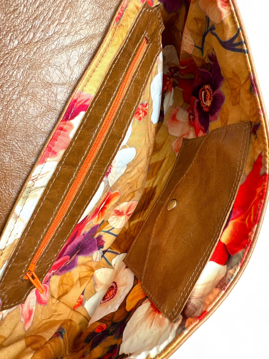 Interior view of the Bronte clutch bag by Lilly & Jude. It shows the floral lining fabric, leather trimmed zipper pocket and the signature integrated leather purse