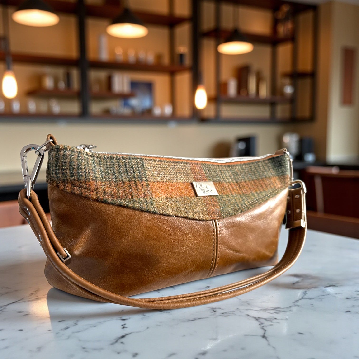 Hand crafted Brown leather and plaid, woollen tweed fabric handbag on a marble surface with a blurred indoor background