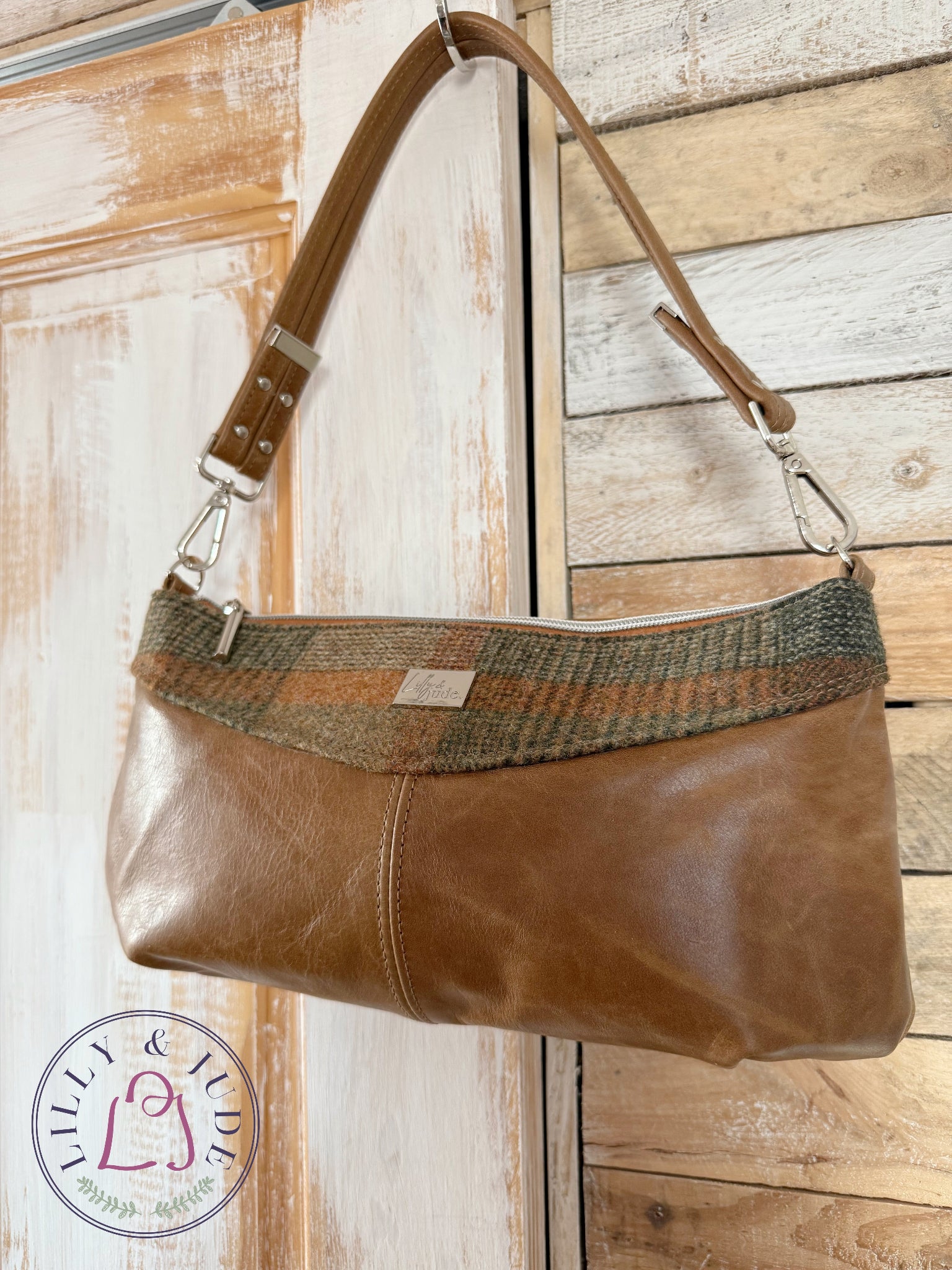 Elland handbag in tan leather and tweed hanging on rustic door with silver hardware.
