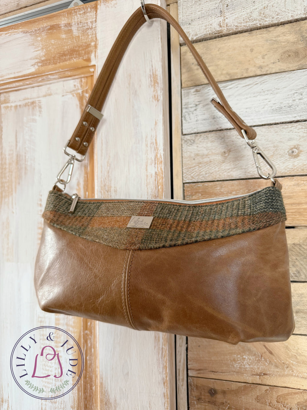 Elland handbag in tan leather and tweed hanging on rustic door with silver hardware.