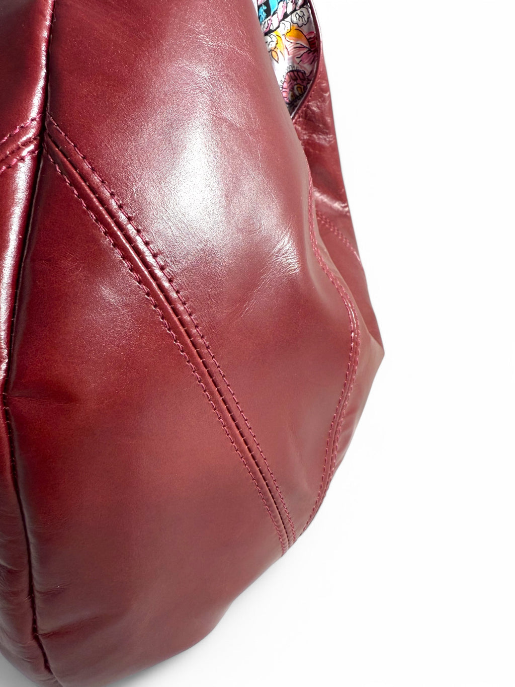 Close-up of the stitching on a deep red leather bag on a white background