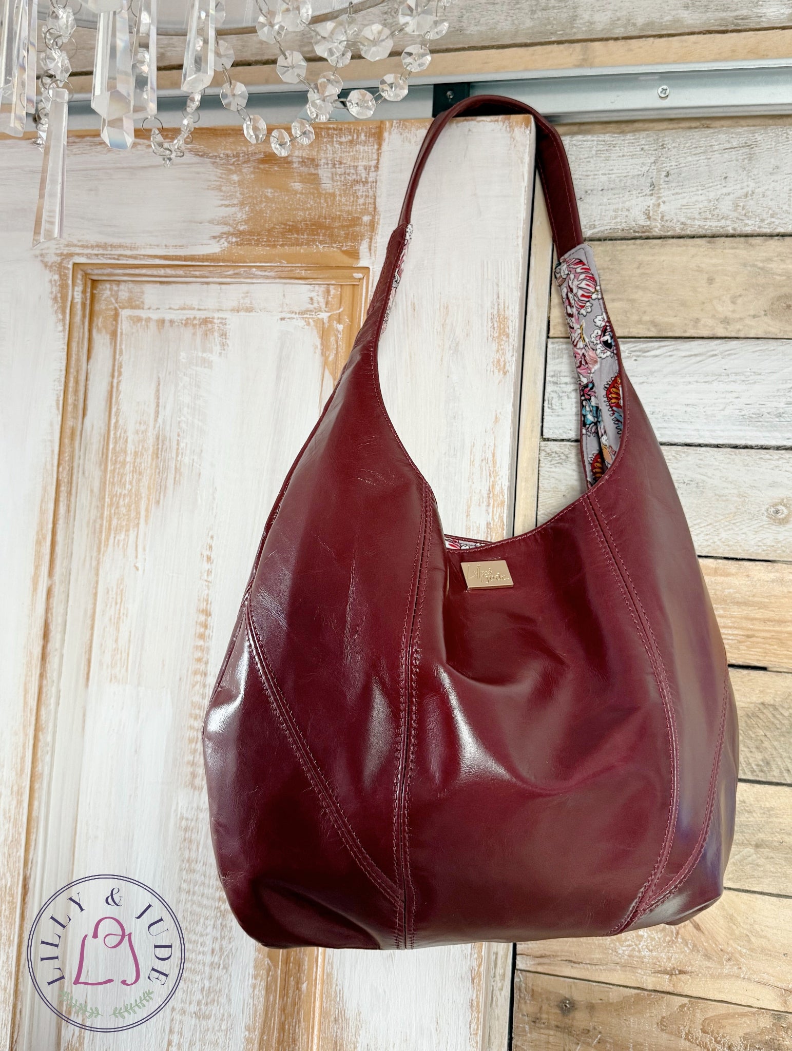 Burgundy leather slouchy handbag hanging against a wooden background.