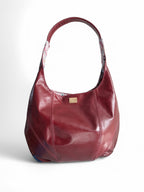 A burgundy slouch tote bag with a leather trim and a small brand tag attached to the side.