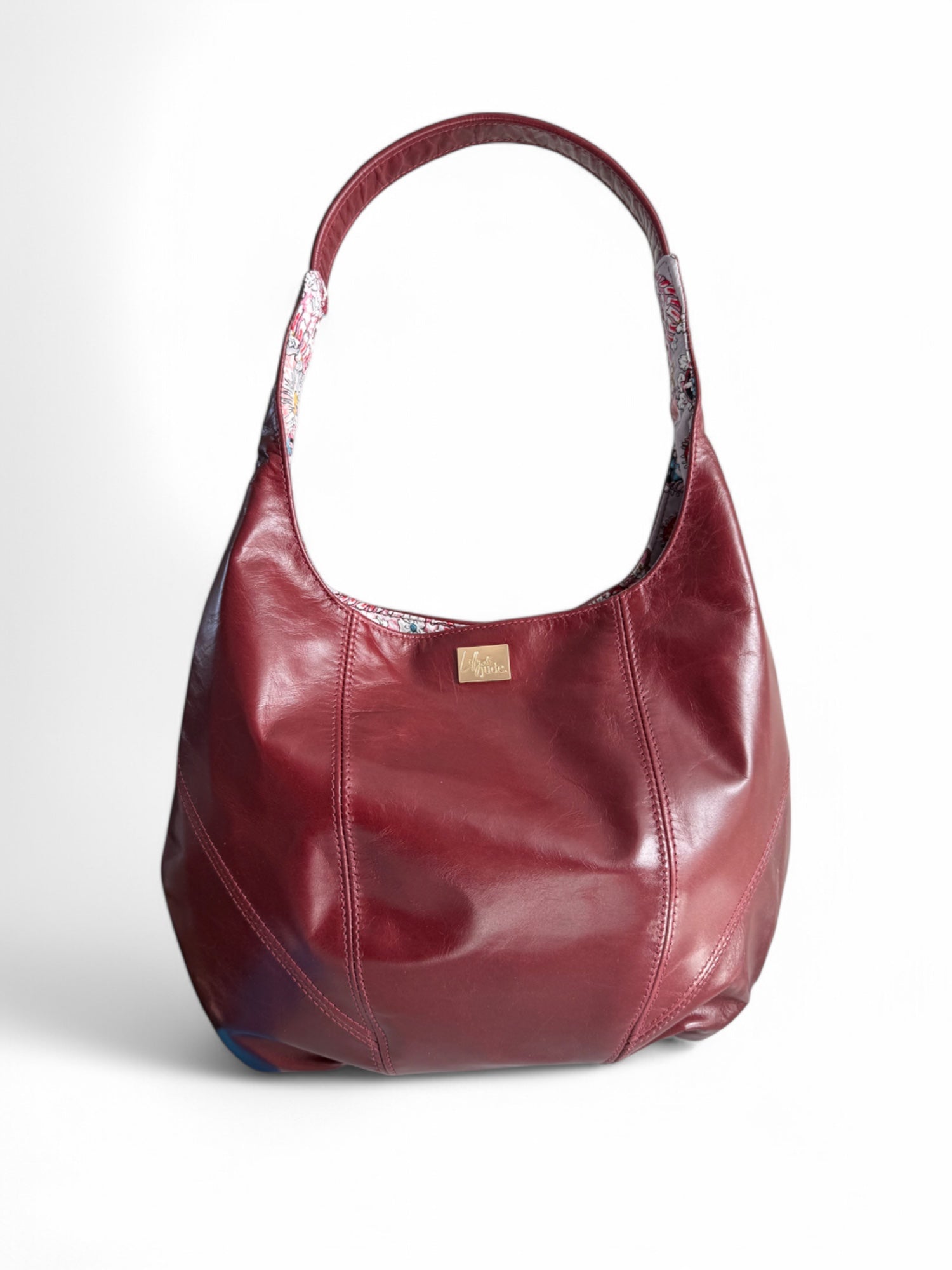 A burgundy slouch tote bag with a leather trim and a small brand tag attached to the side.