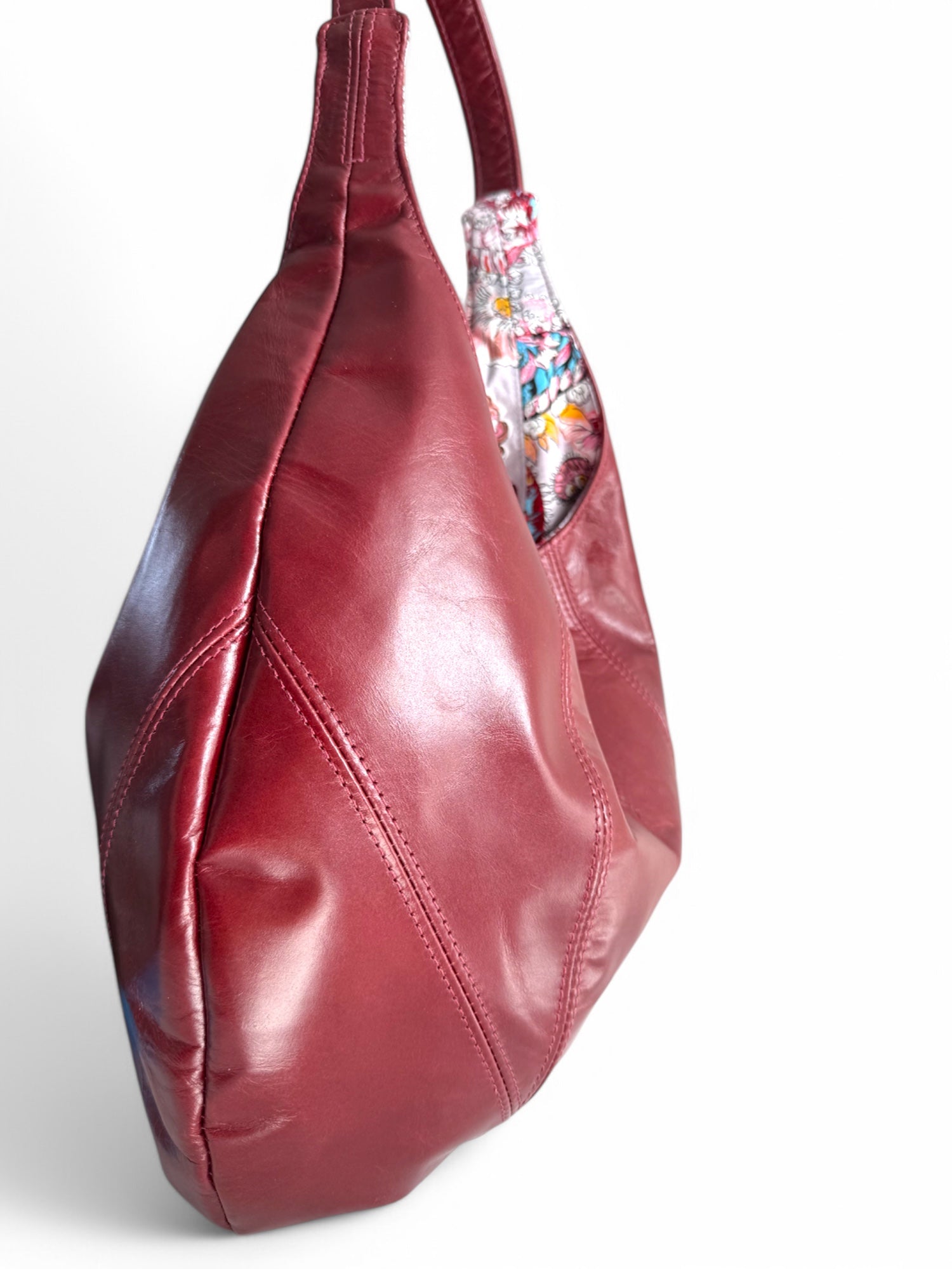 Side view of a dark red leather handbag with paisley patterned lining on a white background