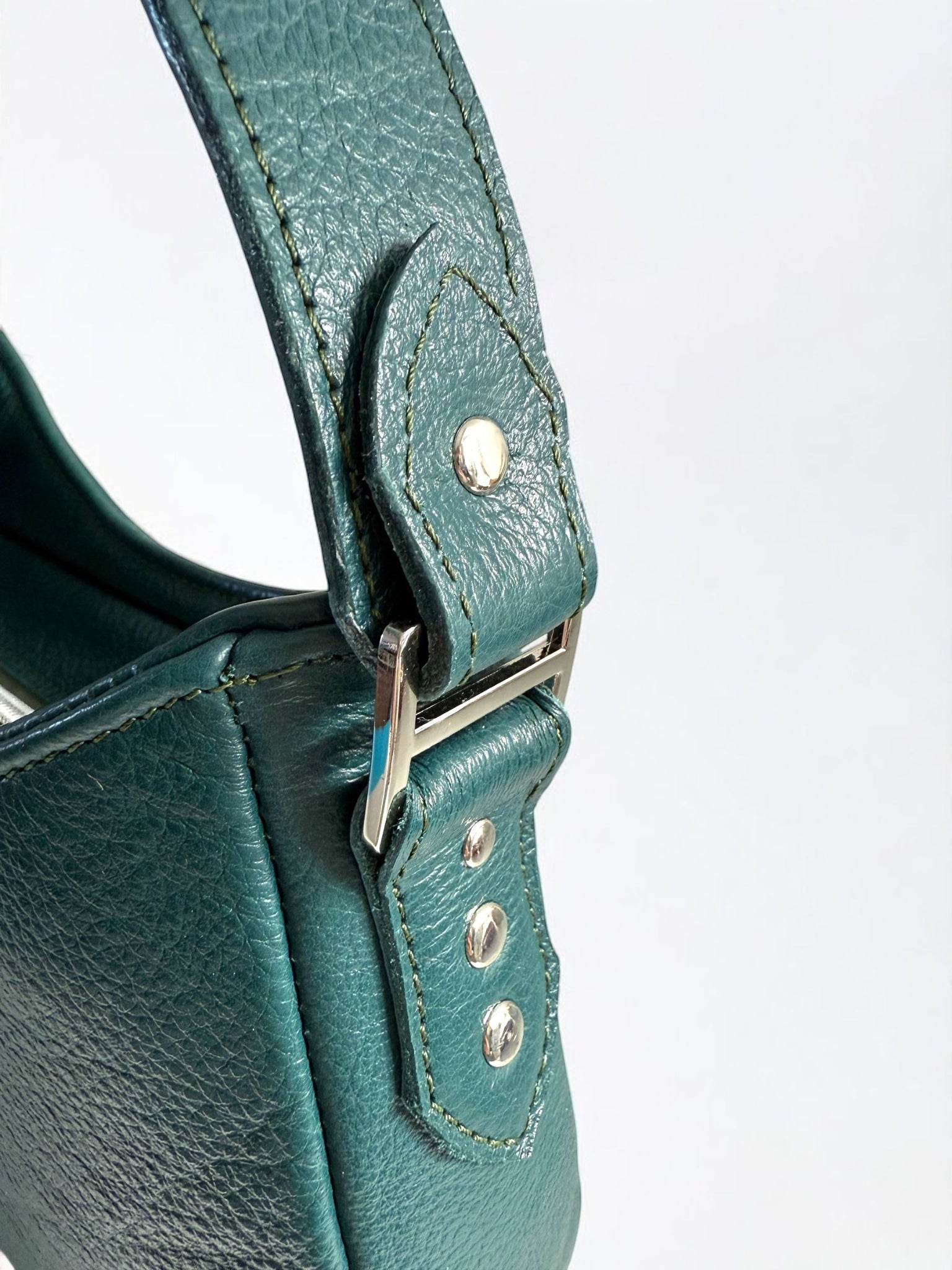 Close-up of a teal handbag's strap and silver buckle strap connector on a white background.