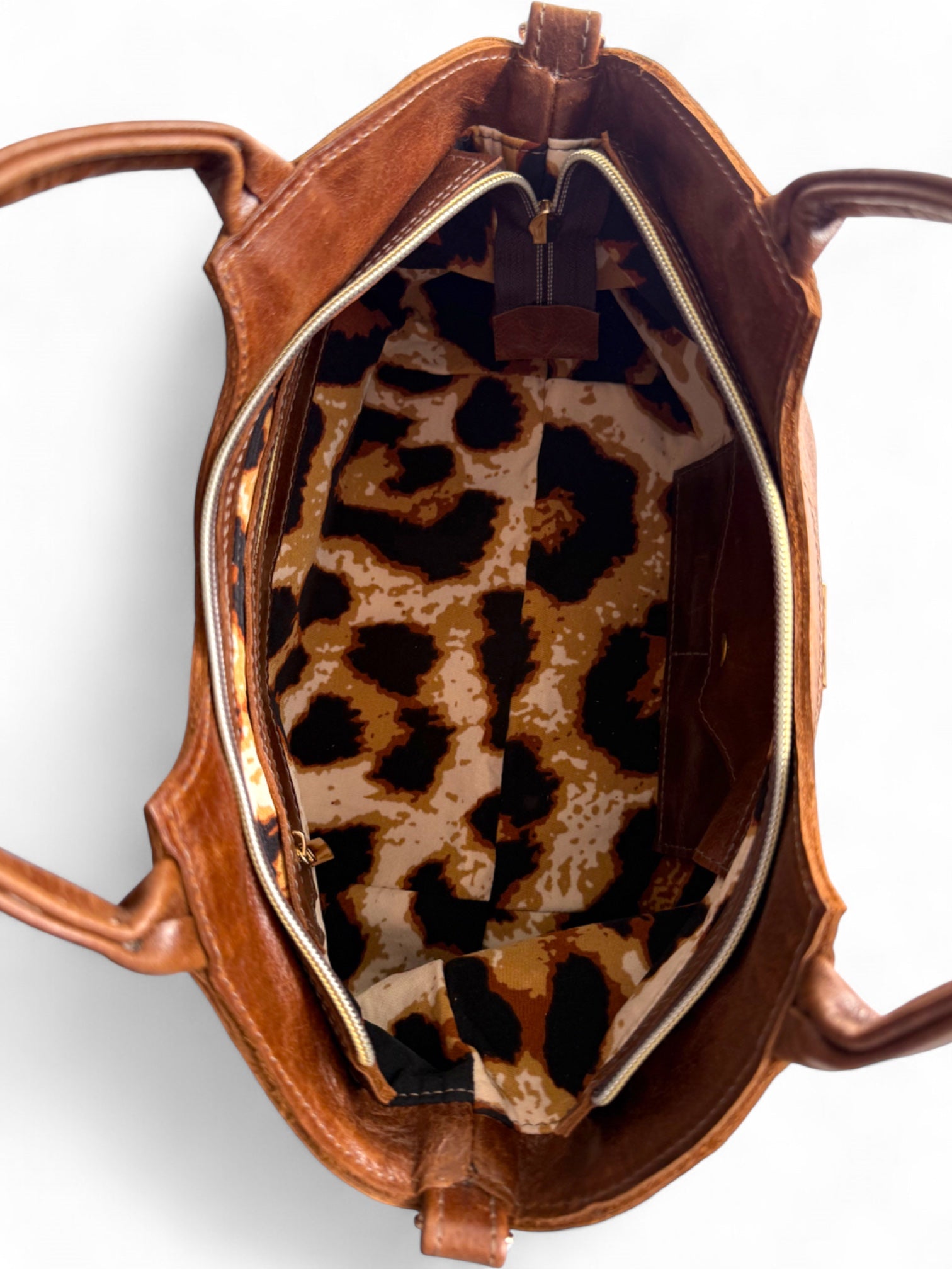 Birds Eye view of the open, brown leather Flossy bag with a leopard print interior on a white background
