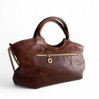 Rear view, showing the zipper pocket of a sustainable, handcrafted, brown leather handbag with a gold zipper on a white background. 