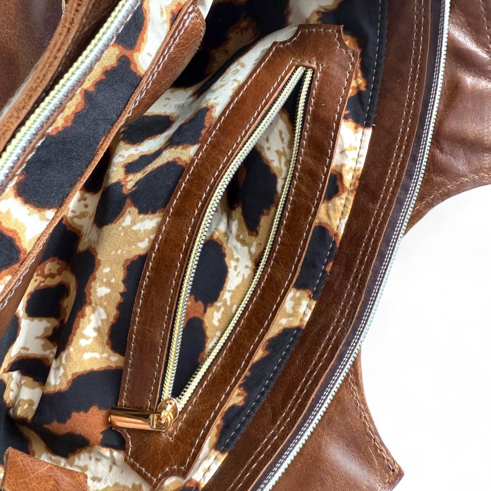 Close-up of the inside of the brown leather Flossy handbag with a zipped compartment and leopard print lining.