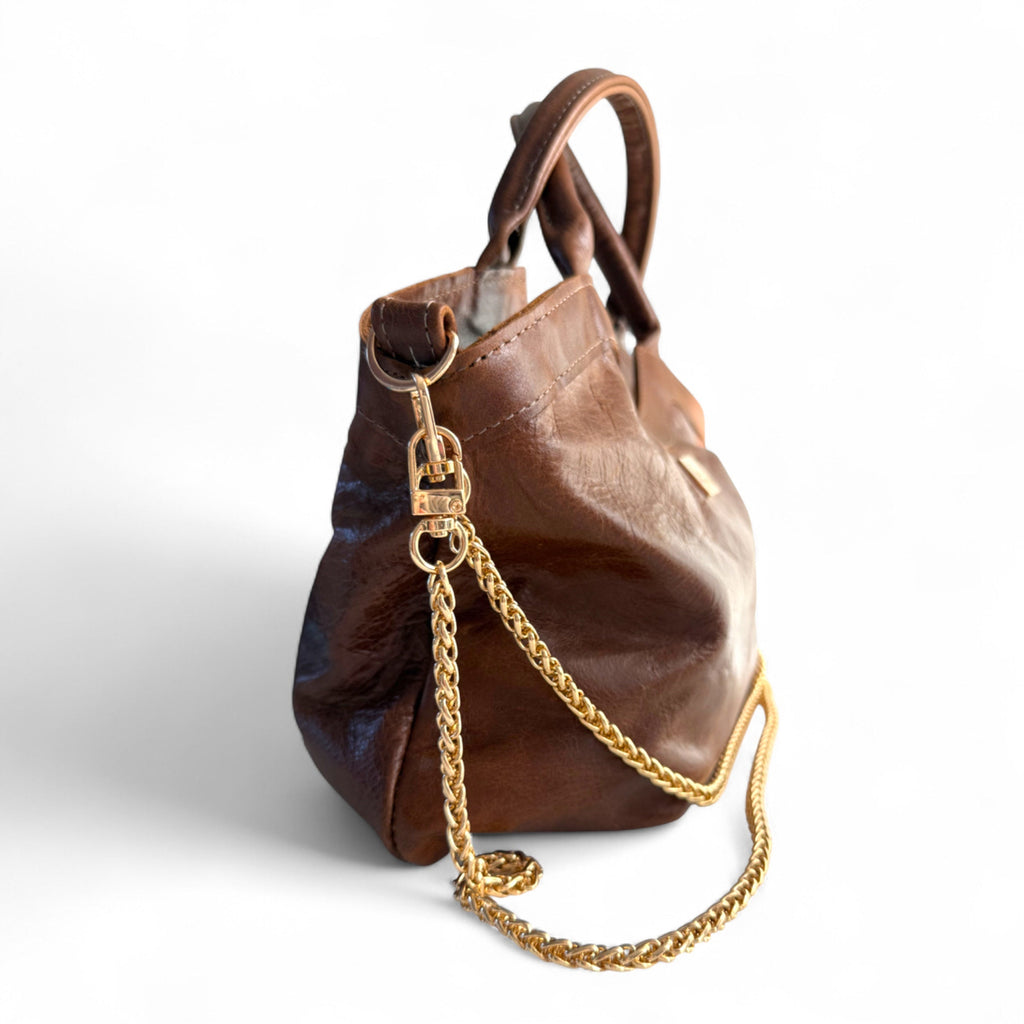 Side view of a chocolate brown leather handbag, with a gold chain on a white background.