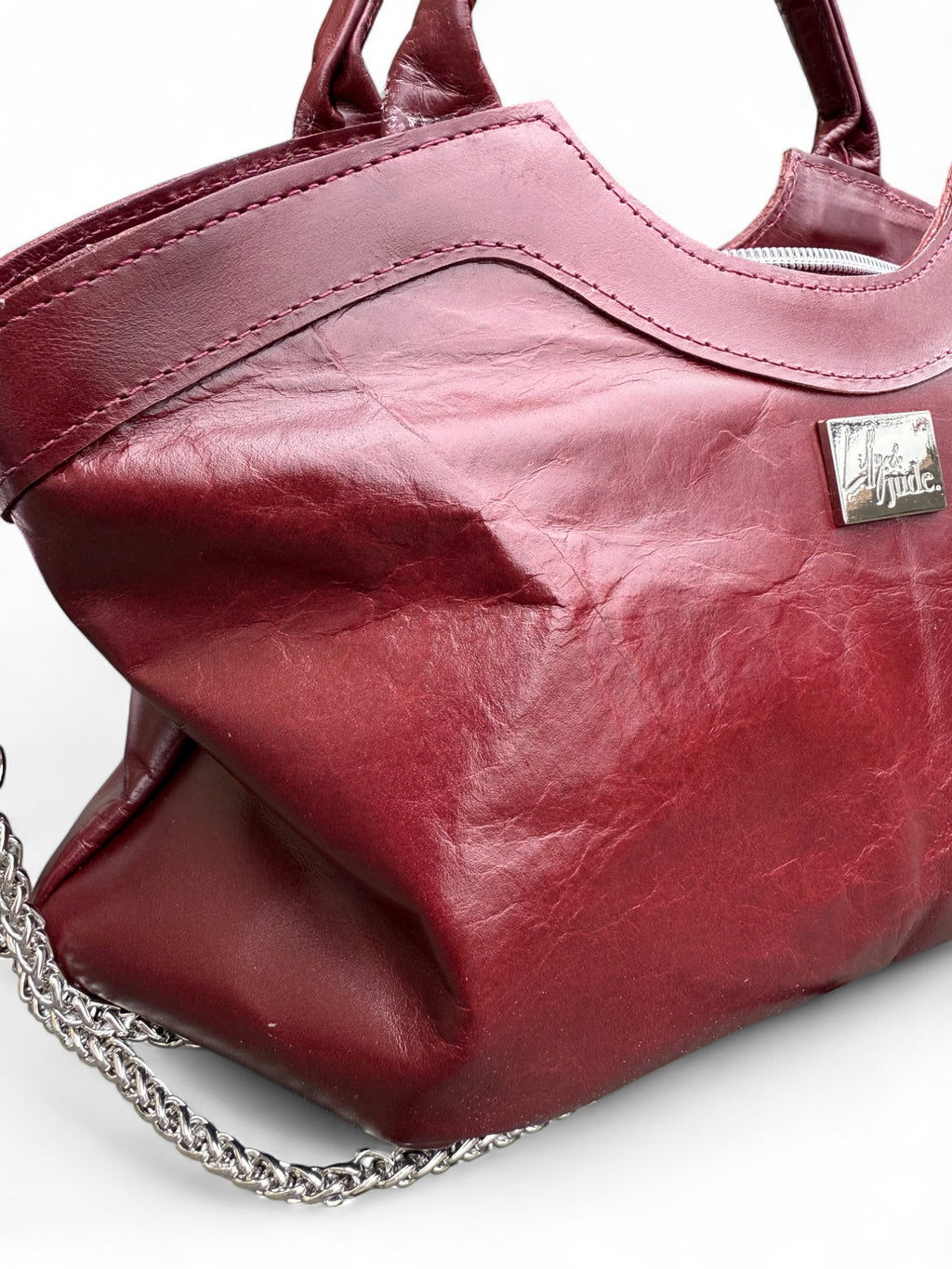 Dark red leather handbag with a silver chain detail on a white background. Showing creases and beauty of the rescued Italian leather and the stitching on the bag