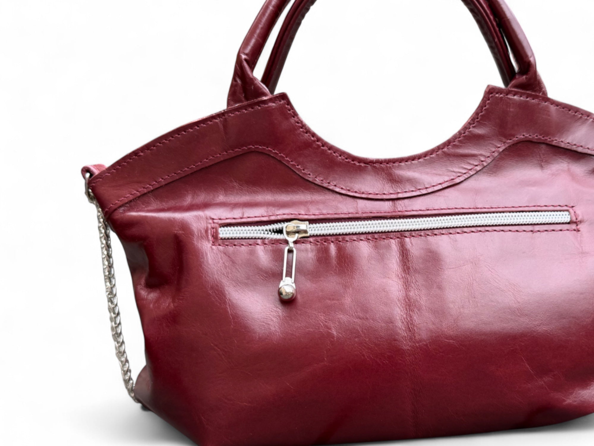 View of the back of the burgundy Flossy handbag, highlighting the silver zipper pull on the back, exterior pocket.