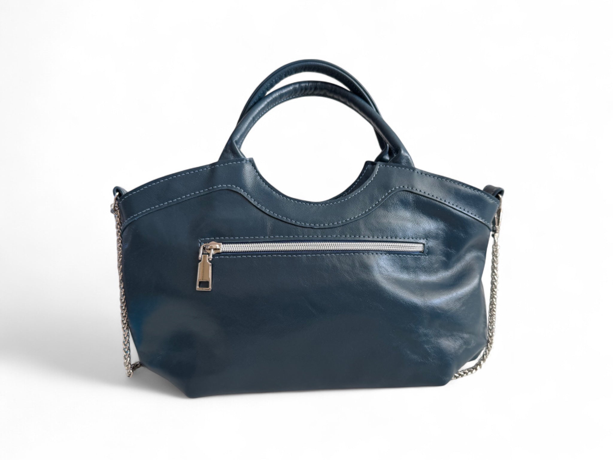 View of the back of the genuine, navy blue  leather Flossy handbag, showing the zipper pocket and a silver chain 