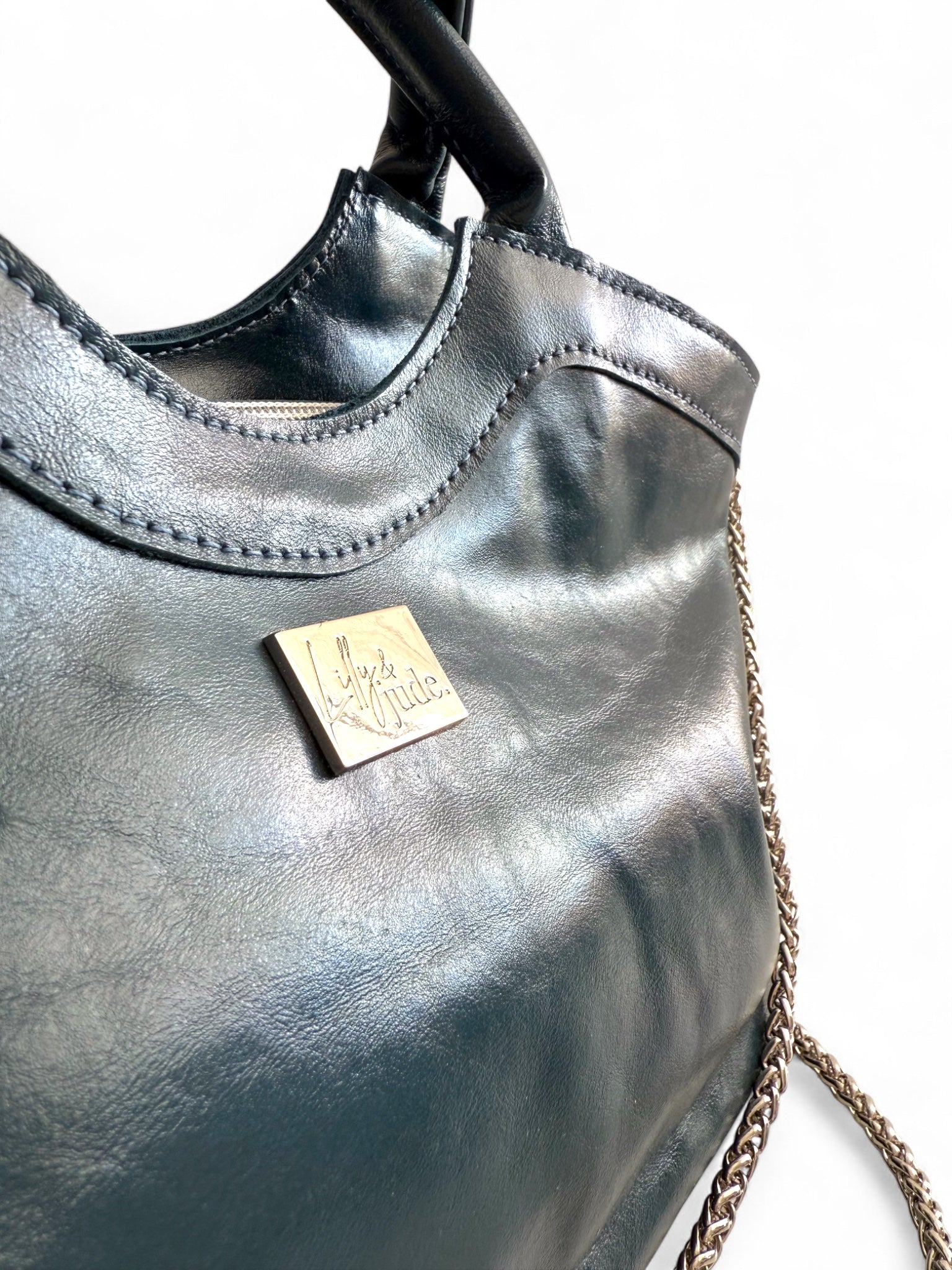 Closeup view of the navy blue Flossy handbag highlighting the texture of the leather, the stitching and the silver logo tag.