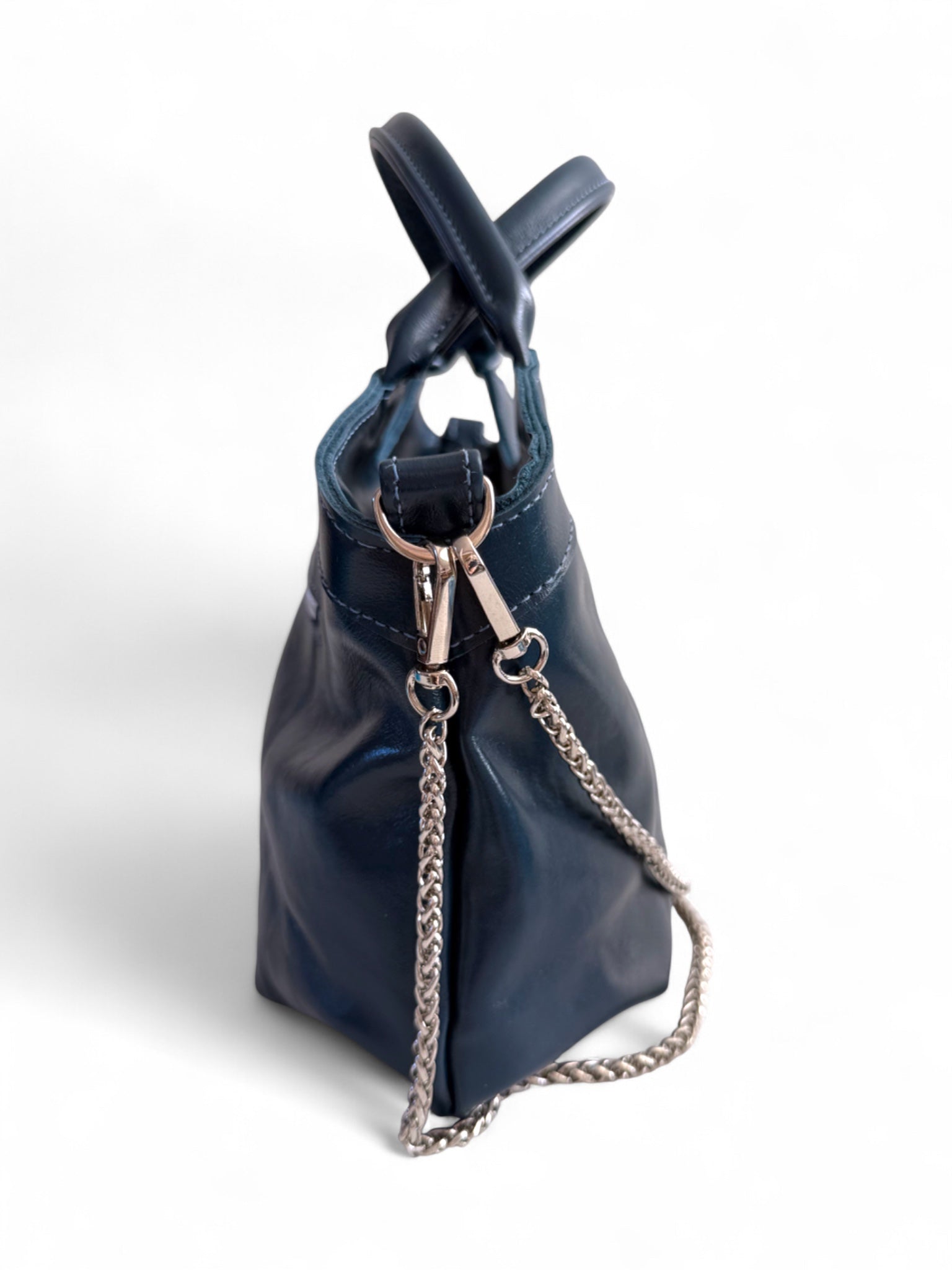 Side view of the navy blue / dark teal rescued leather Flossy handbag with silver hardware and chain detail on a white background