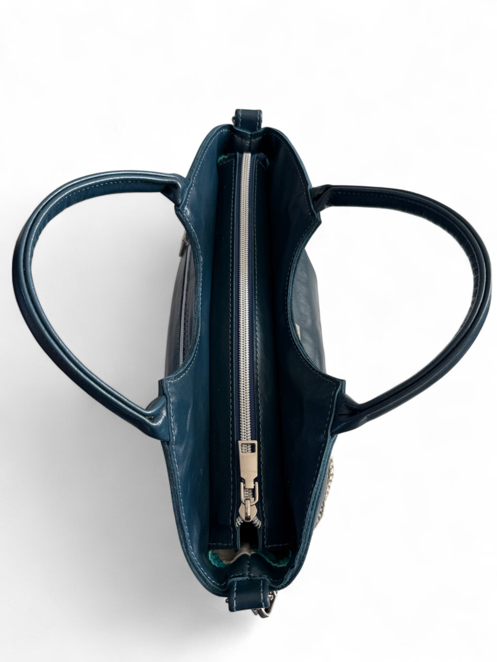 Birds Eye view of the navy blue Flossy bag with silver zipper opening at the top and rolled handles.
