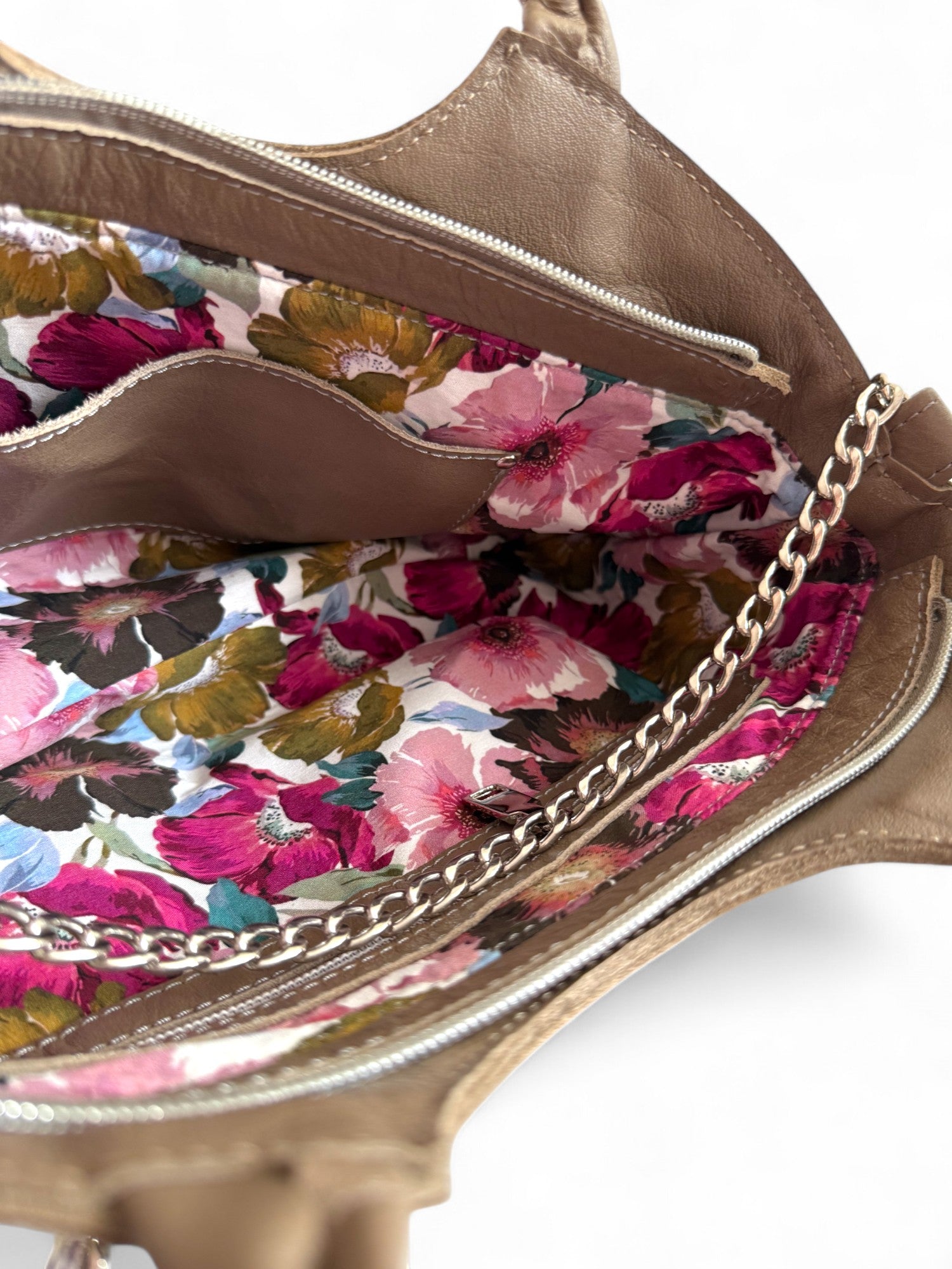 Close-up of a taupe, upcycled leather handbag with floral interior lining and silver chain strap. 