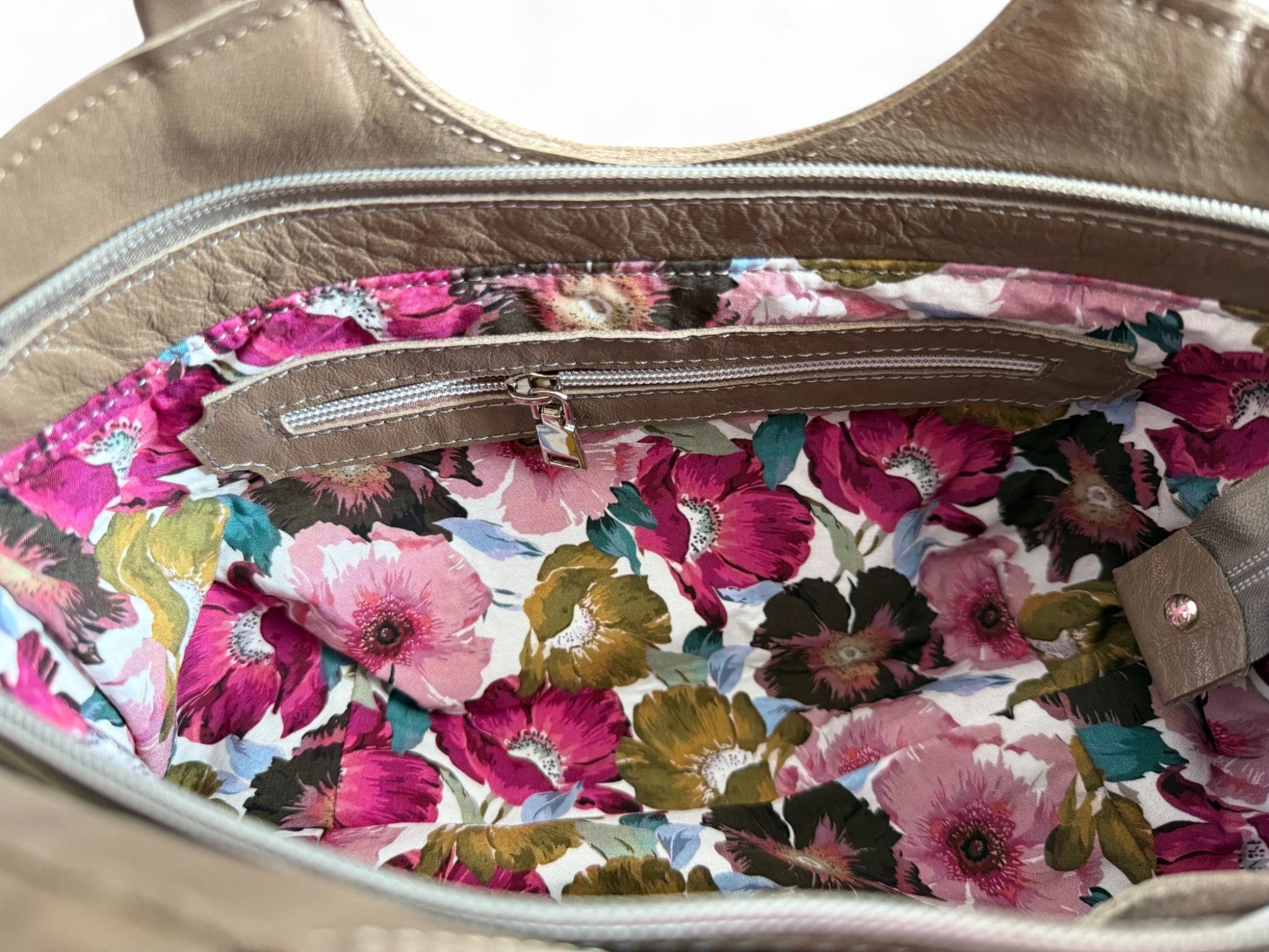 View of the floral interior lining of the taupe leather Flossy bag, with leather trimmed interior zipper pocket.