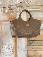 Taupe leather handbag, hanging from the top corner of a wooden door, with a chandelier in the foreground. 