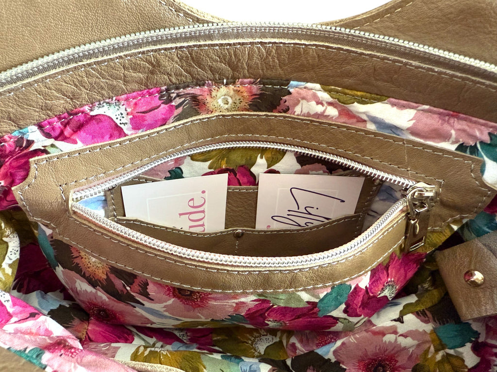 View of the interior zipper pocket of the taupe leather Flossy handbag, with floral lining and integrated purse. 