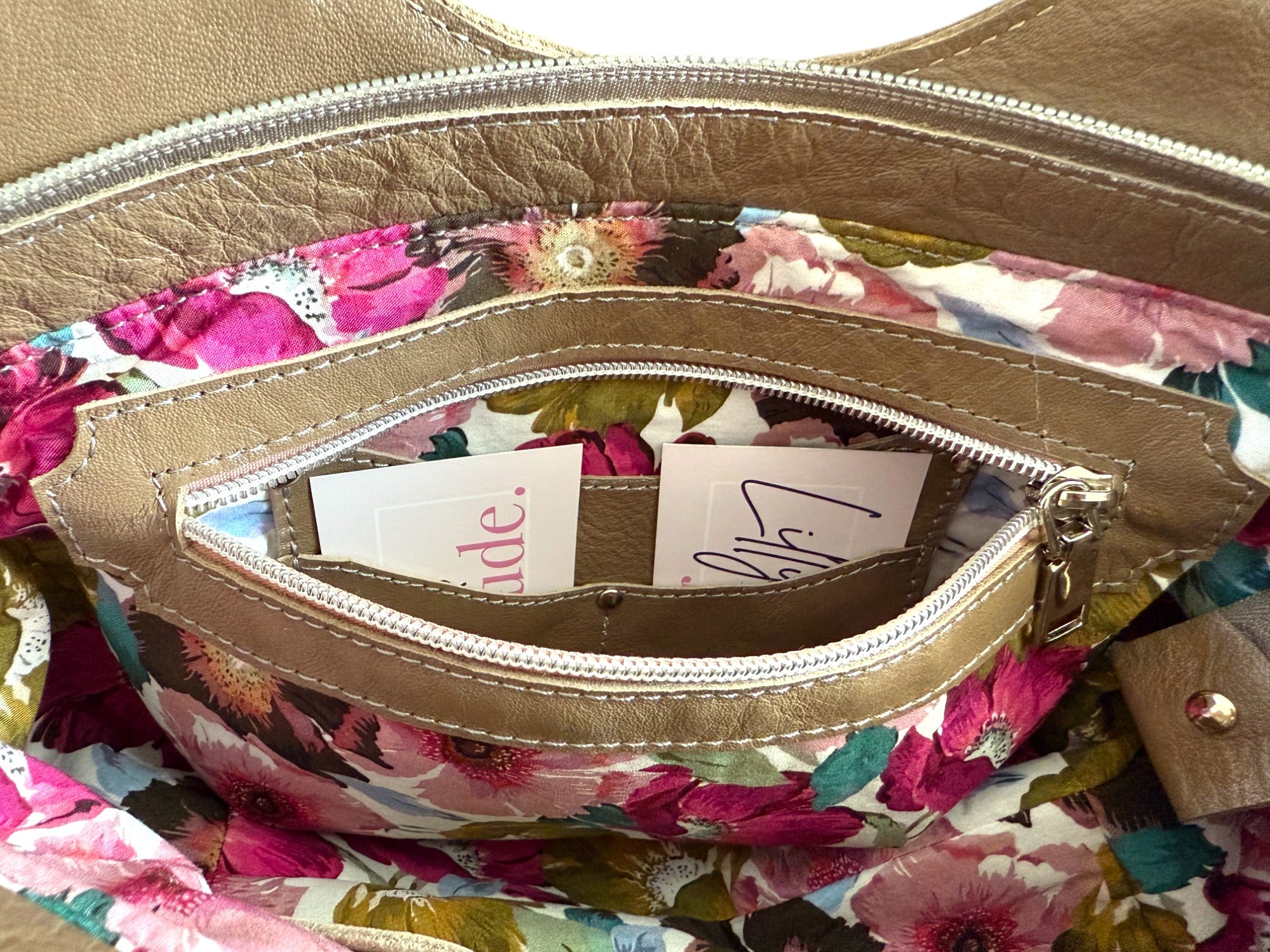 View of the interior zipper pocket of the taupe leather Flossy handbag, with floral lining and integrated purse. 