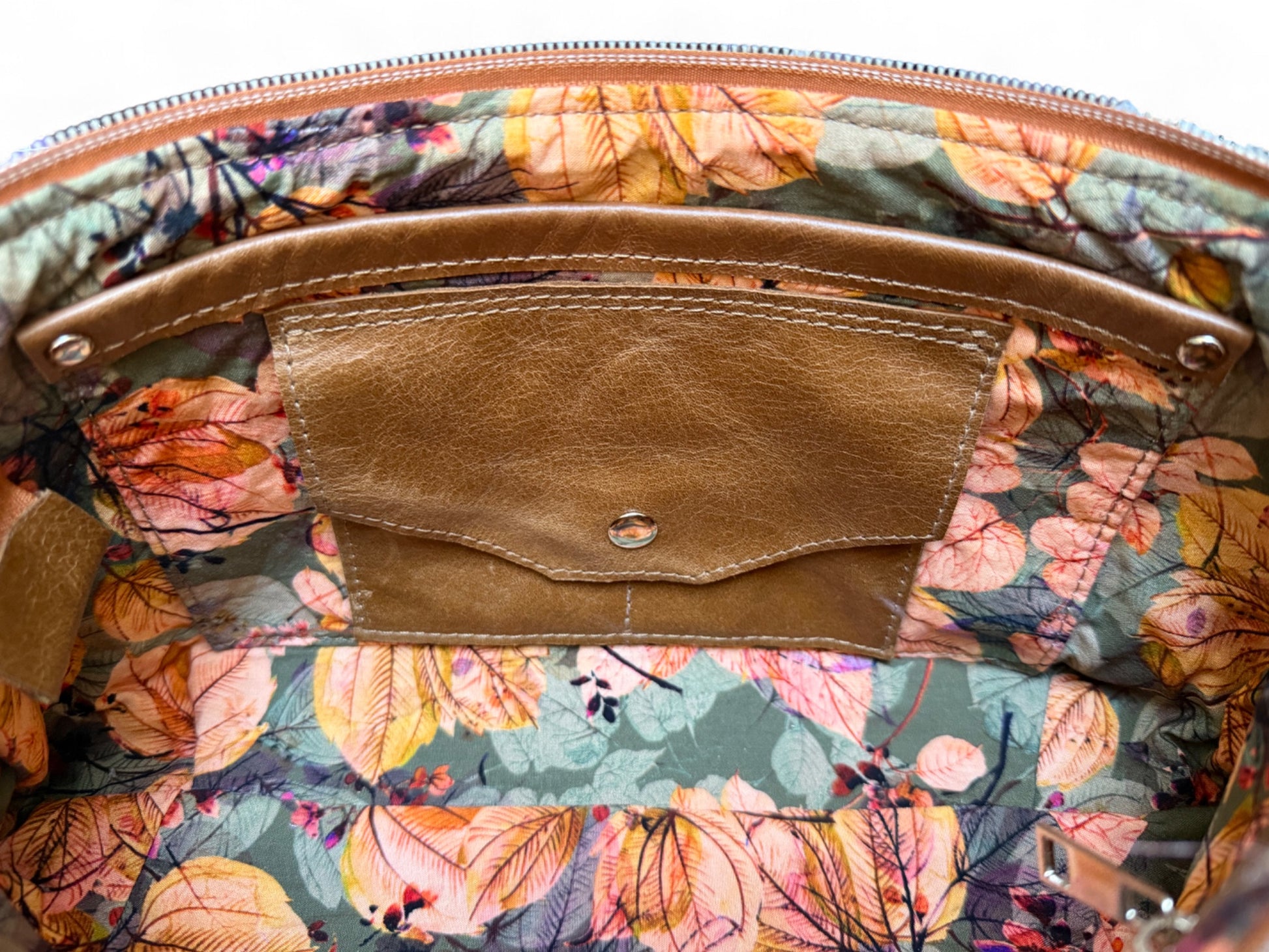 Interior view of Elland handbag. The fabric is khaki, orange and tan coloured floral patterned. The view shows a leather trimmed slip pocket and integrated leather purse