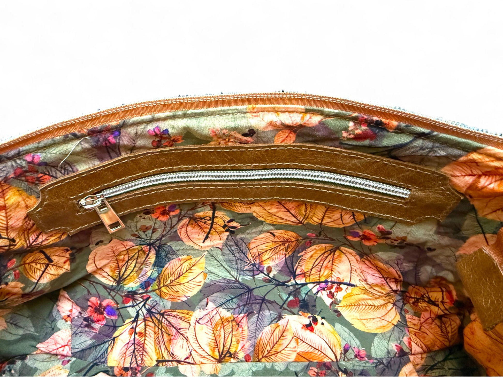 Floral-patterned bag with a zipper on a white background. Interior view of leather East / West Handbag