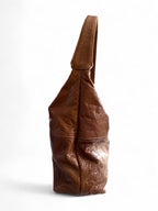 Side view of a tan brown leather slouchy shoulder bag on a white background