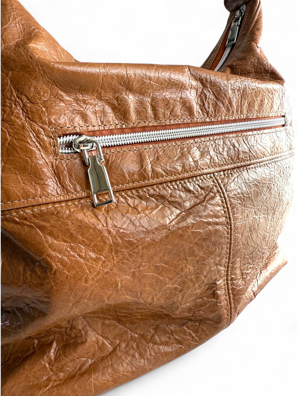 Tan brown leather handbag with a zipper on a white background