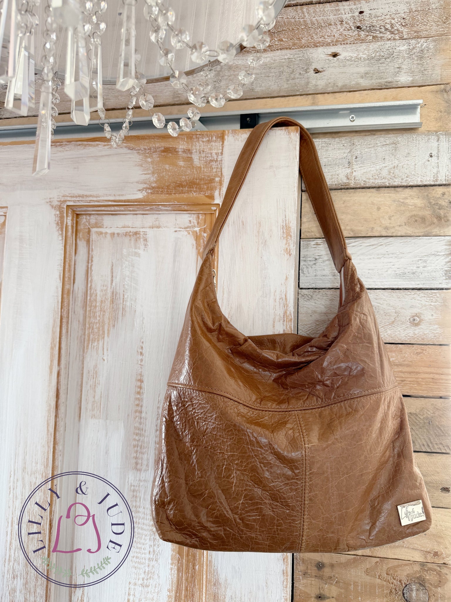 Brown leather handbag hanging on a wooden door with a chandelier in the background