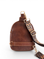 View of the back of a brown leather sling bag, showing the two strap connectors on either side, showing where you can connect the patterned strap.