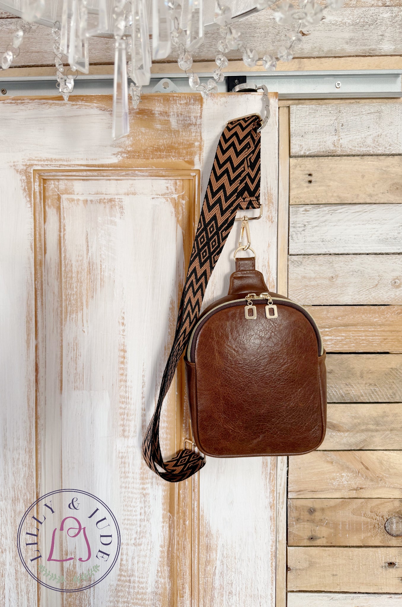 Handmade, brown leather sling bag with a patterned strap hanging from a wooden door