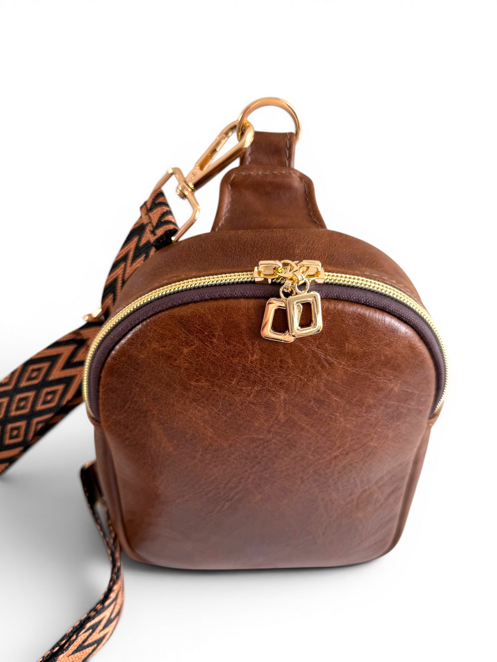 Top view of the Maven sling crossbody bag, in brown leather with gold zipper on a white background