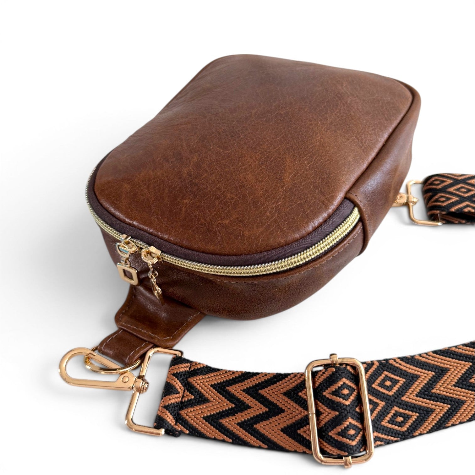 A small, brown leather sling bag with a patterned strap, lying on a white background
