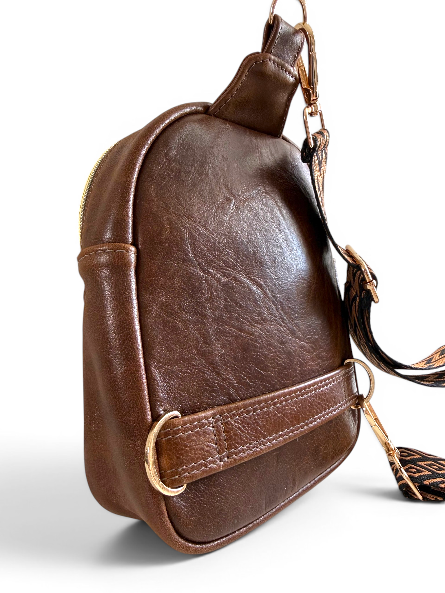 View of the back and side of a brown leather crossbody bag with gold hardware and a patterned strap on a white background