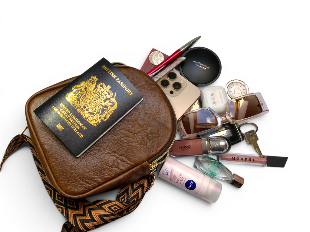Brown leather travel bag with passport, makeup items, and keys pilling out, on a white background