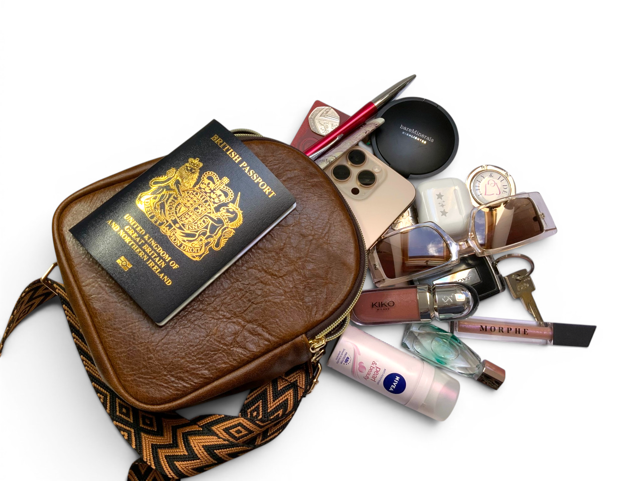 Brown leather travel bag with passport, makeup items, and keys pilling out, on a white background
