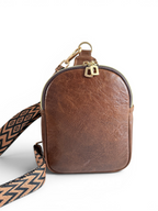 Brown leather crossbody sling bag with a patterned strap and gold hardware on a white background