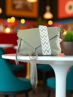 Light green handbag with a matching pale olive green and white chevron patterned, crossbody strap. on a white table in a colourful coffee shop setting. 